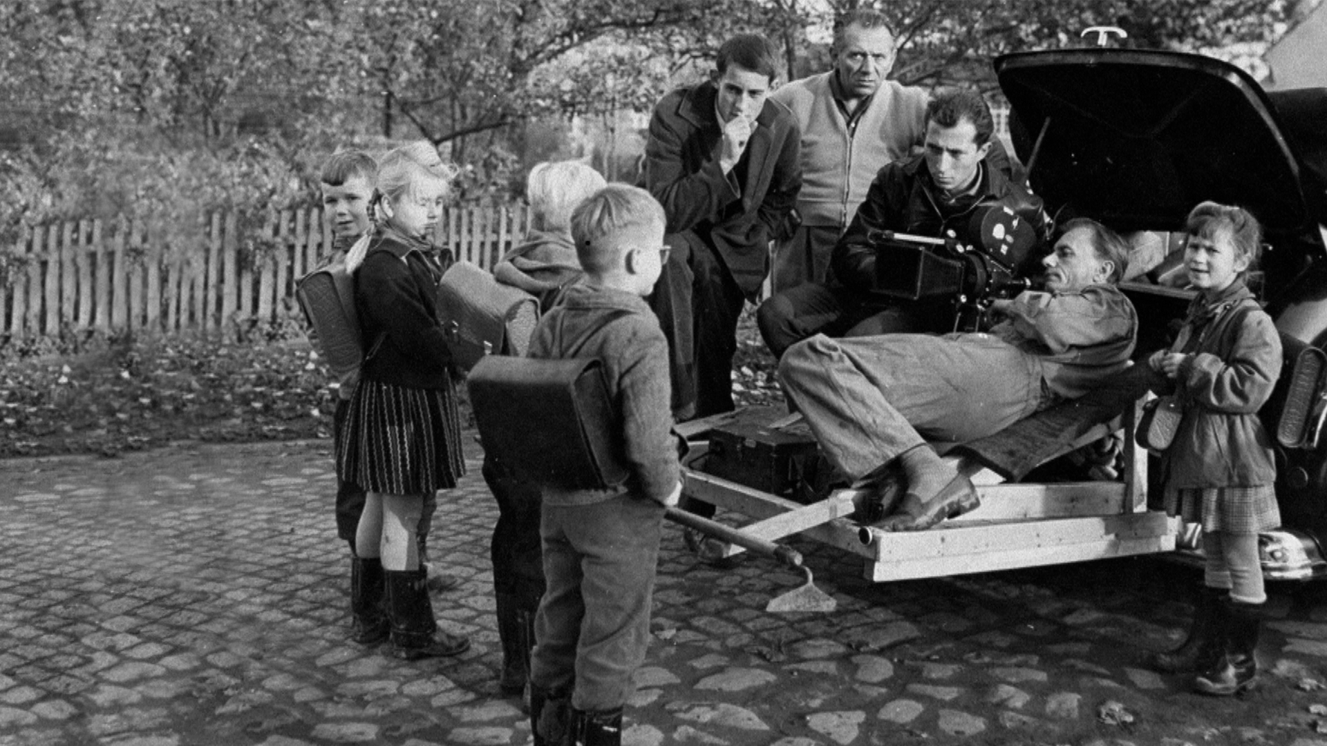 Filmteam u.a. mit Winfried Junge, Kameramann im Auto-Kofferraum/-Anhänger, Erstklässler mit Schulranzen auf Dorfstraße (ca. 1961 in Golzow)
Quelle: rbb/Hans-E. Leupold