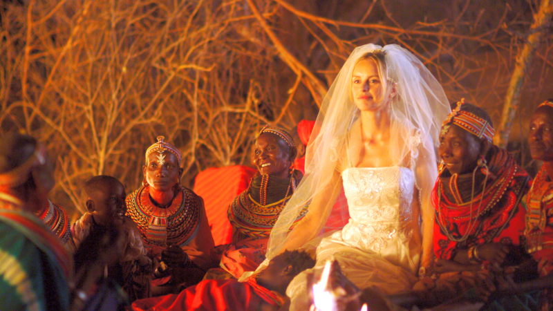 Carola, gespielt von Nina Hoss, sitzt in einem weißen Brautkleid mit Schleier zwischen Angehörigen vom Stamm Samburu.