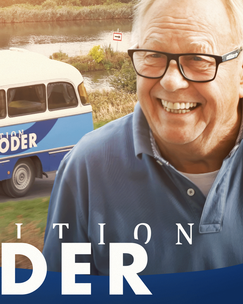 Im Vordergrund lacht Reinhard Rogge, im Hintergrund ist der hintere Teil seines himmelblauen Robur-Busses zu sehen.