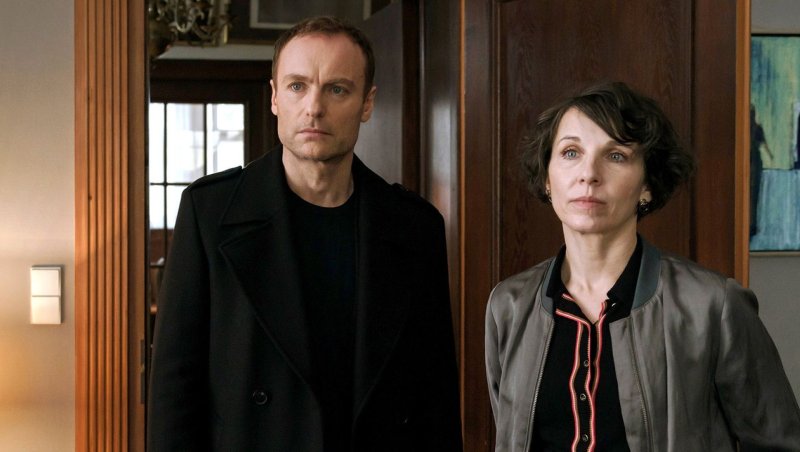 Zwei Ermittler:innen stehen im TĂĽrrahmen einer Wohnung und schauen ernst nach vorn.