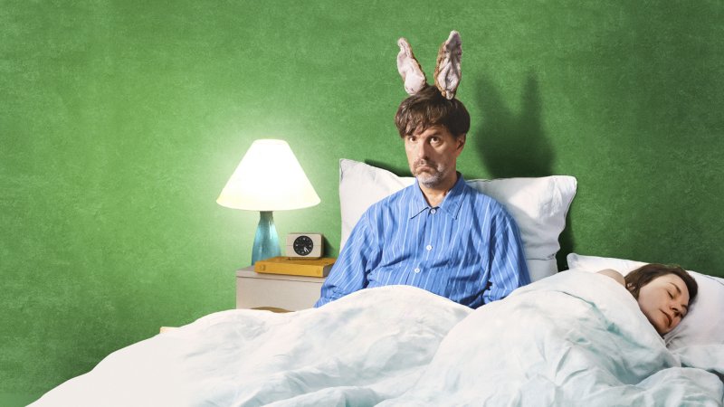 Christoph Maria Herbst trägt Hasenohren und einen Pyjama und sitzt im Bett. Neben ihm liegt Christiane Paul.