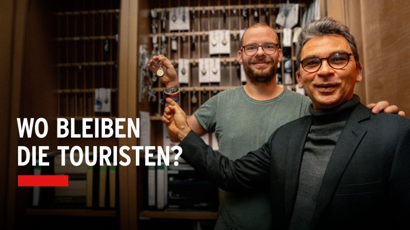 Vater und Sohn vom Hotel Kastanienhof stehen vor einem Schlüsselbrett in der Rezeption; einer hält einen Hotelschlüssel hoch.