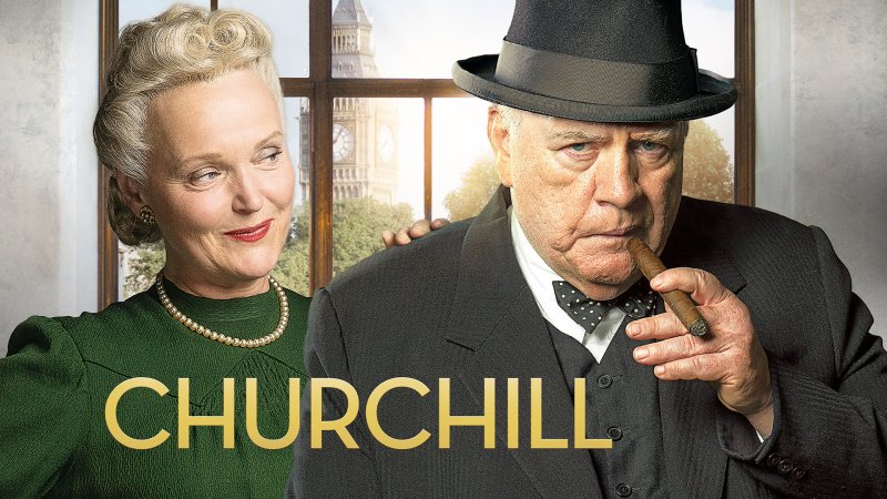 Brian Cox als Winston Churchill mit Zigarre und Hut vor Miranda Richardson als Clemmie Churchill, im Hintergrund Fenster mit Big Ben, (Quelle: rbb/© Salon Churchill Ltd)