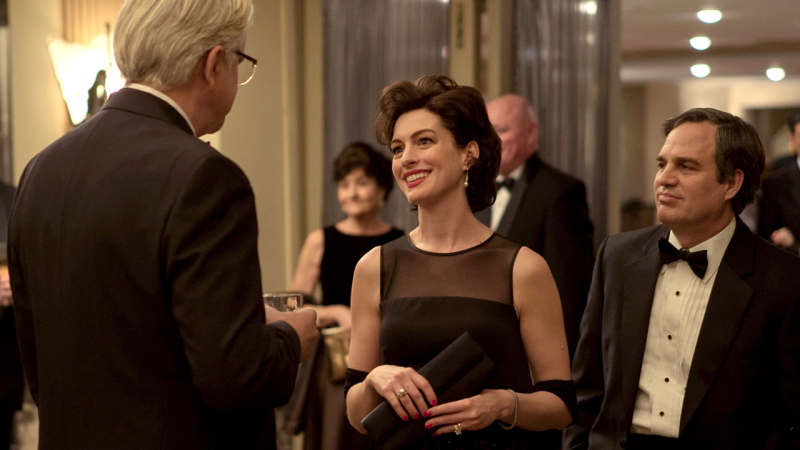 Anne Hathaway ist als Anwaltsgattin bei einem festlichen Anlass neben ihrem Mann Robert Bilott (Mark Ruffalo) zu sehen und lächelt eine Person, die mit dem Rücken zur Kamera steht, an.