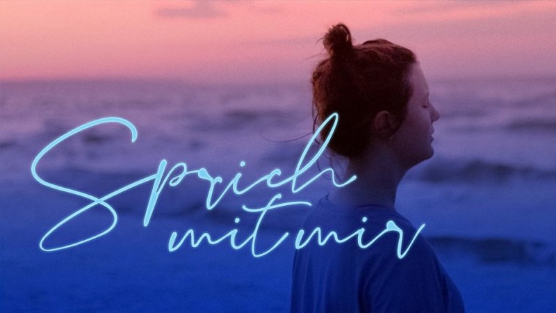 Eine Frau steht im Profil am Meer im Abendlicht.