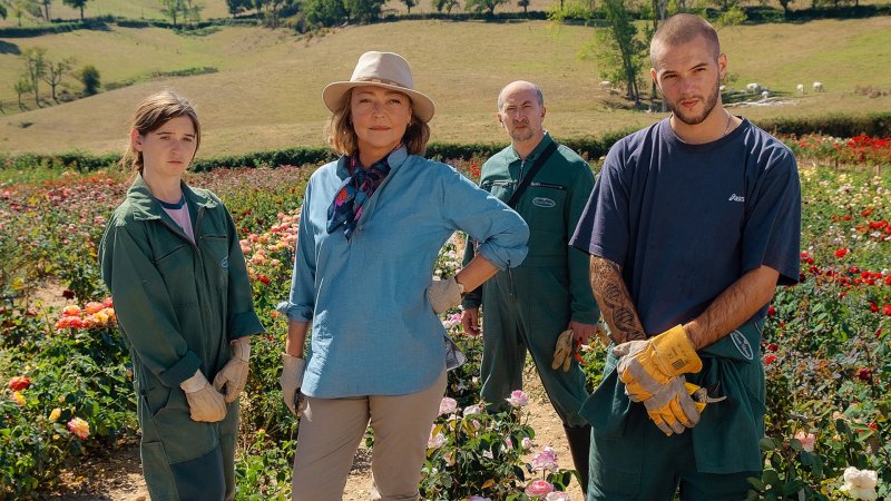 Vier Menschen stehen zwischen blühenden Rosenfeldern, darunter Madame Vernet mit Hut und drei Mitarbeiter in Arbeitskleidung.