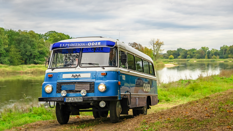 Ein blauer Robur fährt auf einem Feldweg entlang eines Flussufers, (Quelle: rbb/Norman Gäbler)